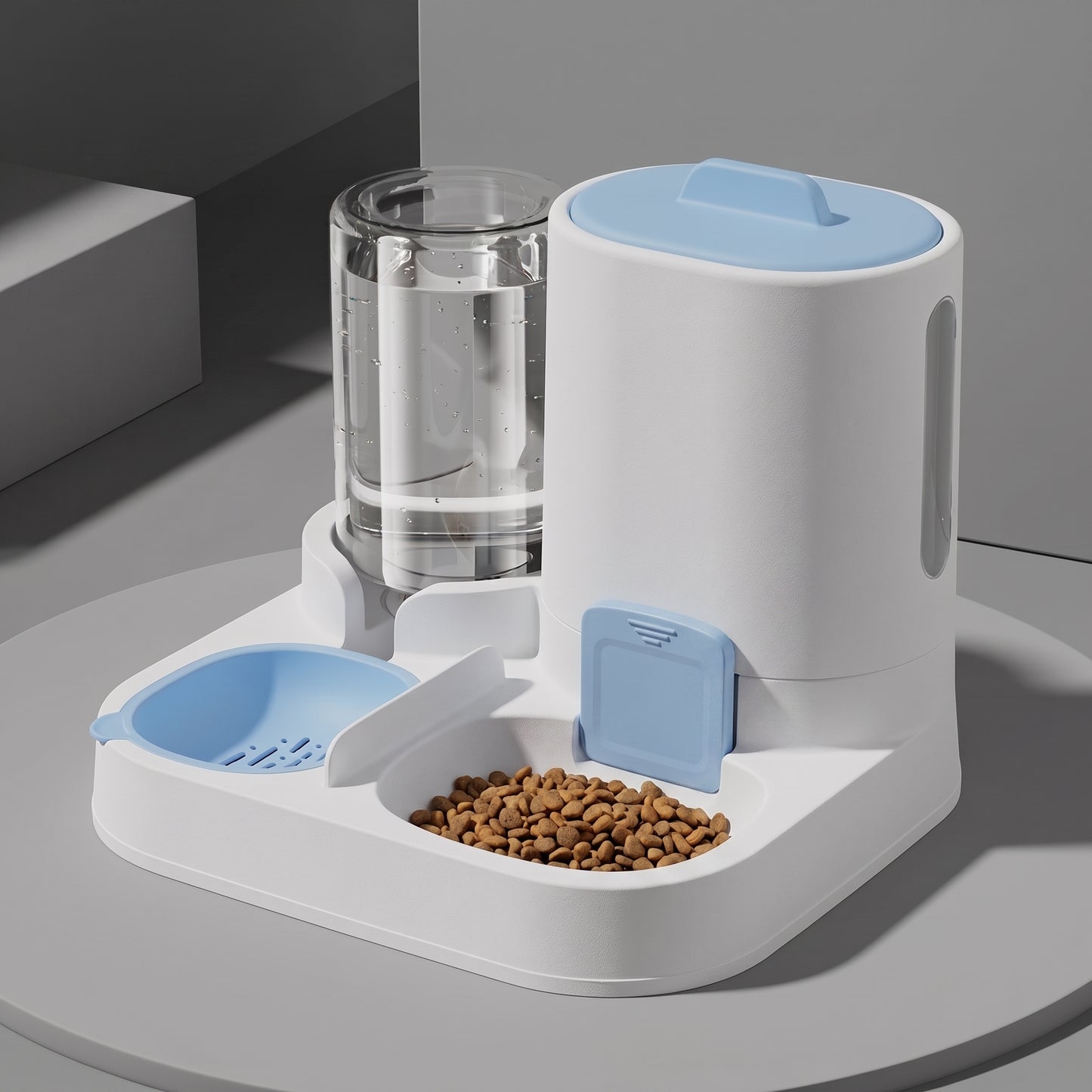 A white automatic pet feeder and water dispenser with light blue accents, shown on a round gray table. The feeder includes a clear water reservoir, a bowl of kibble, and a blue food hopper.