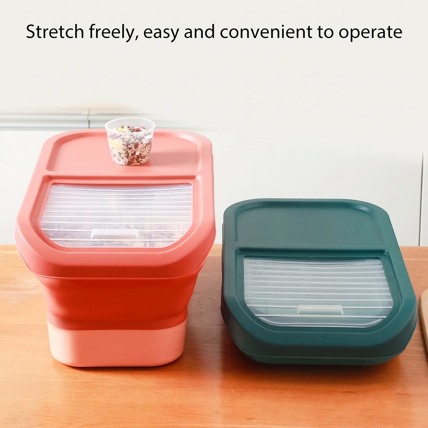 Two collapsible food storage containers shown on a wooden surface against a light wall, with text at the top reading 'Stretch freely, easy and convenient to operate.' One container is coral pink and one is dark teal; both have translucent slotted lids and are shown closed, with a small clear cup placed on the pink container.