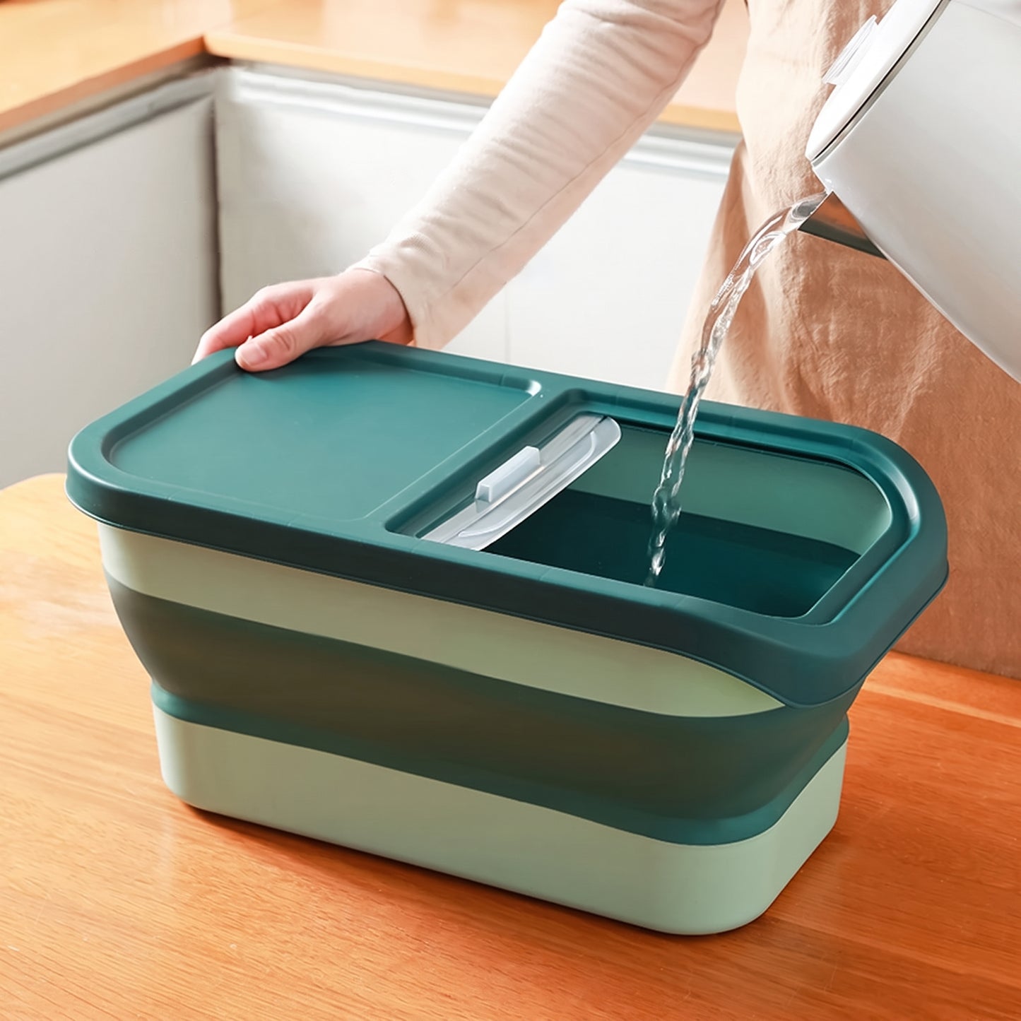 Collapsible green and beige container with water being poured into it on a wooden surface.