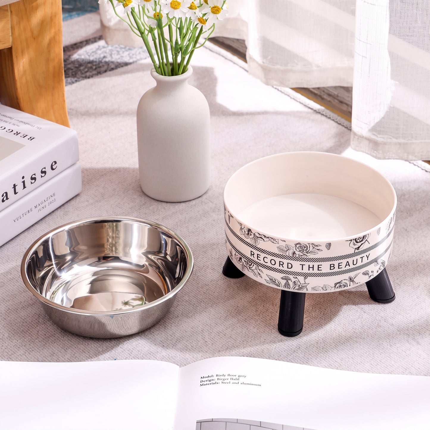 Two bowls, one metallic and one with decorative legs, on a light surface with a vase and books in the background.